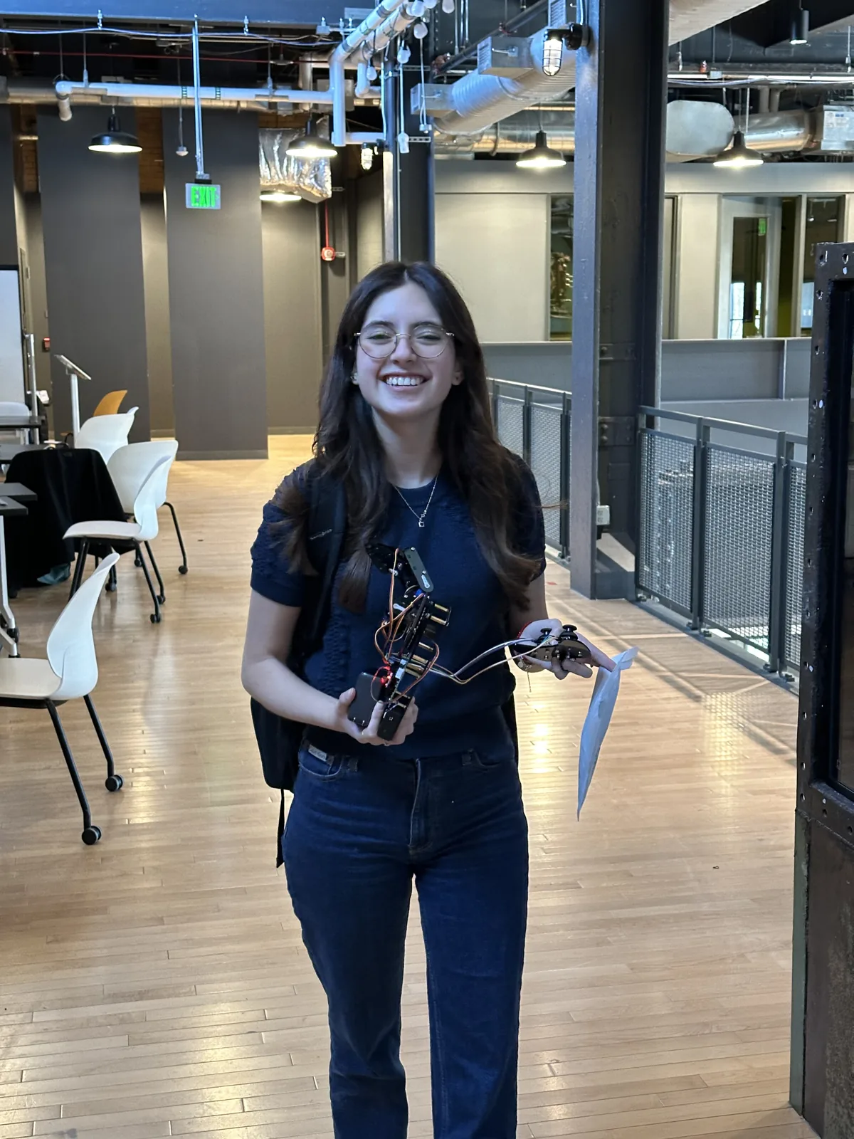 Daniela Ojeda smiling and holding the finished robot arm in the hackathon venue