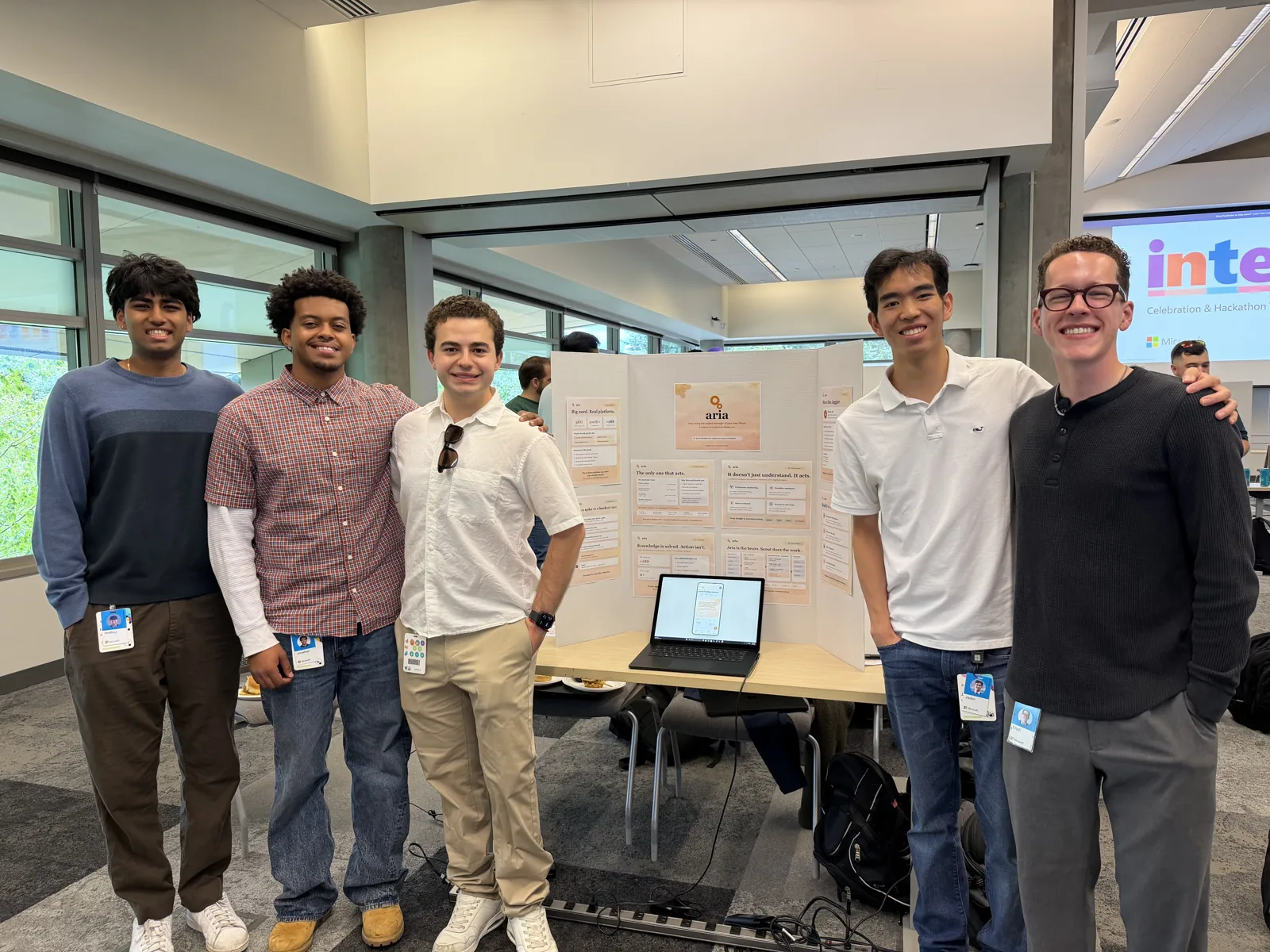 The five-person Aria team standing around their poster and laptop at the Microsoft Global Intern Hackathon