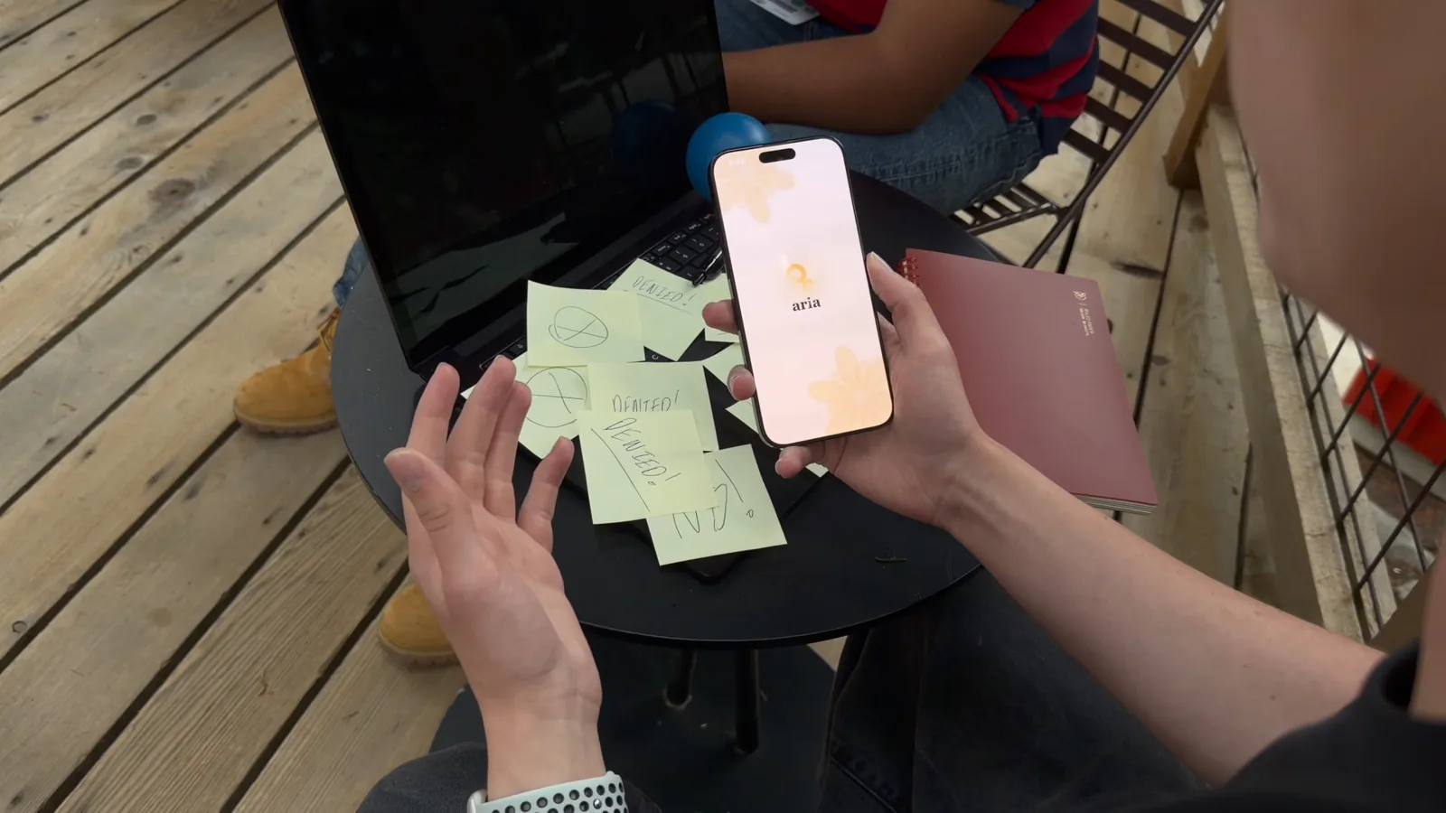 Hands holding a phone with the Aria app open over a table of sticky notes on a wooden deck